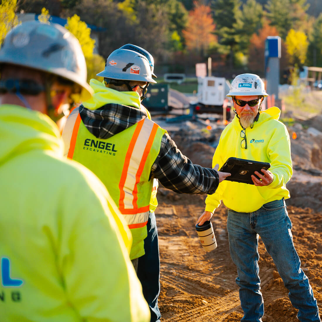Three workers in safety gear reviewing a tablet on site.