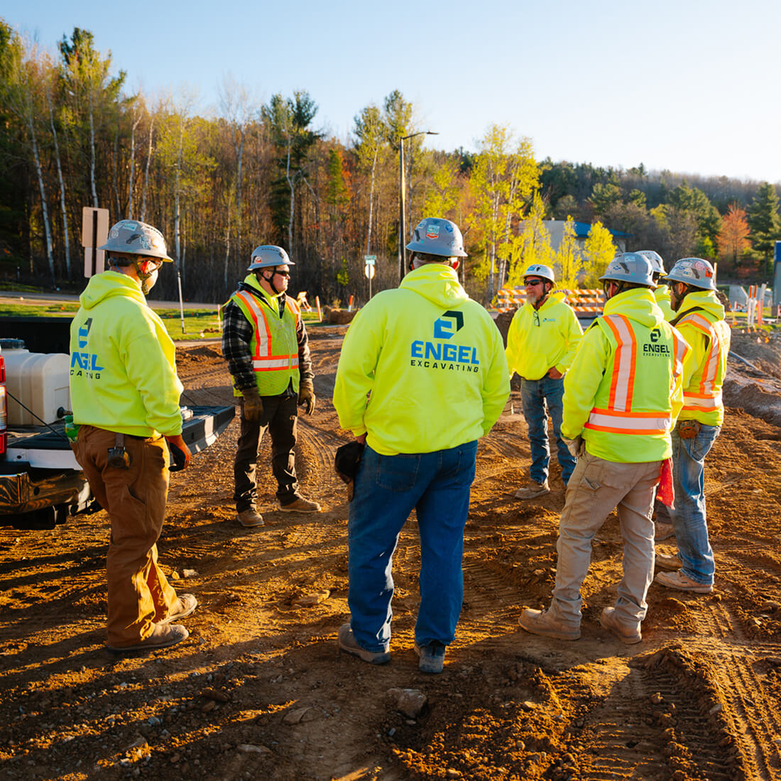 Six builders in safety gear talk on a dirt site.