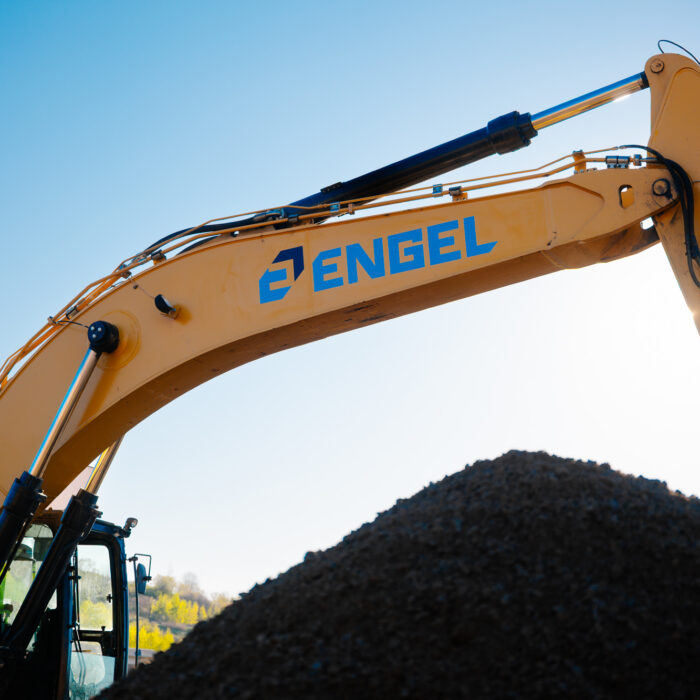 Yellow Engel excavator behind dirt mound, clear sky.