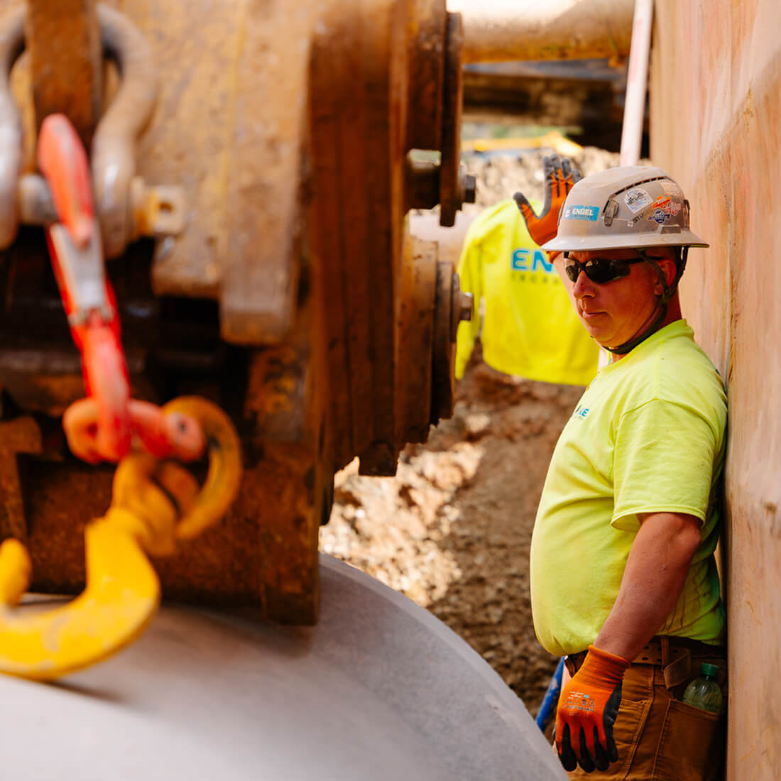 Worker in hard hat stands near machinery and large pipe.