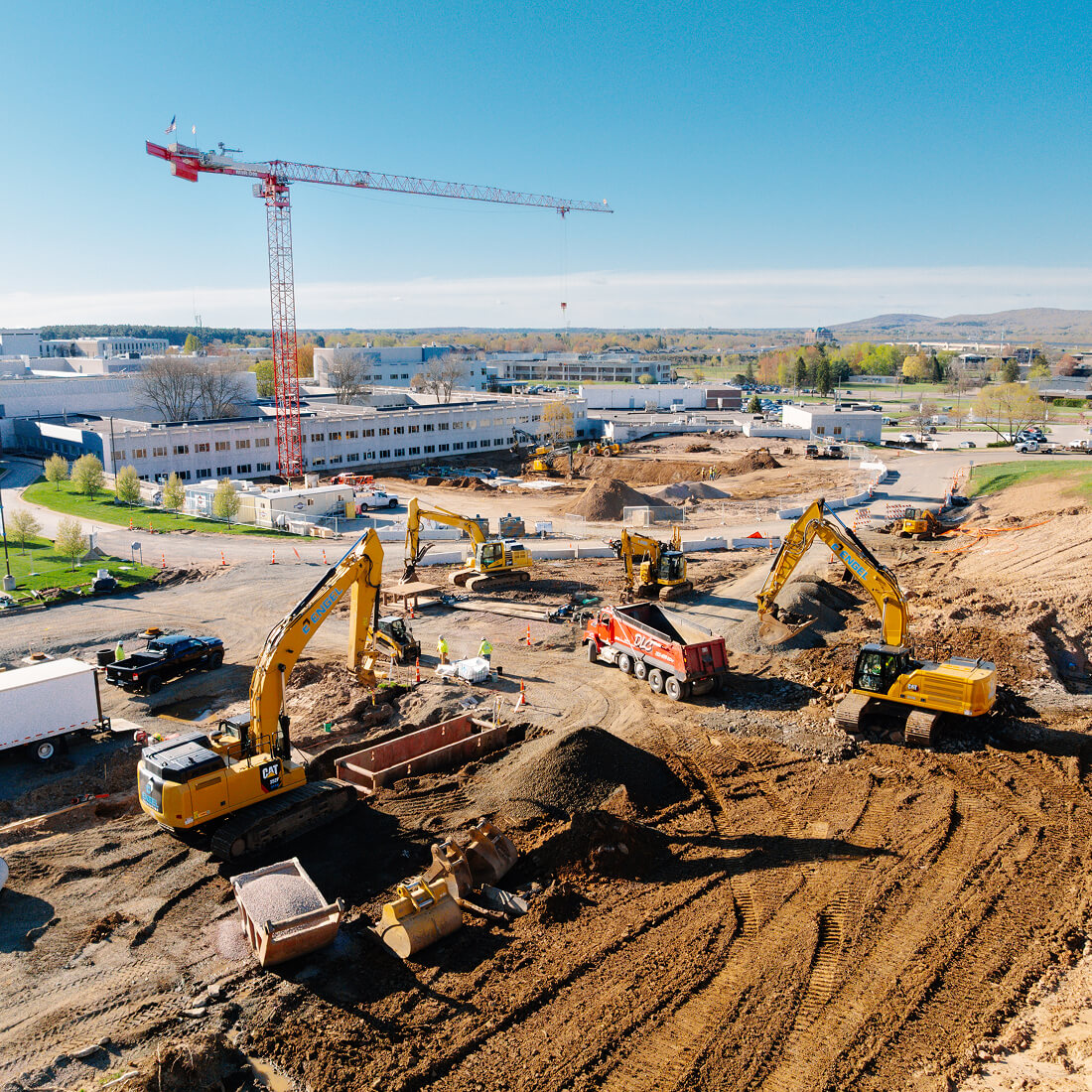 Construction site with excavators, crane, and distant buildings.