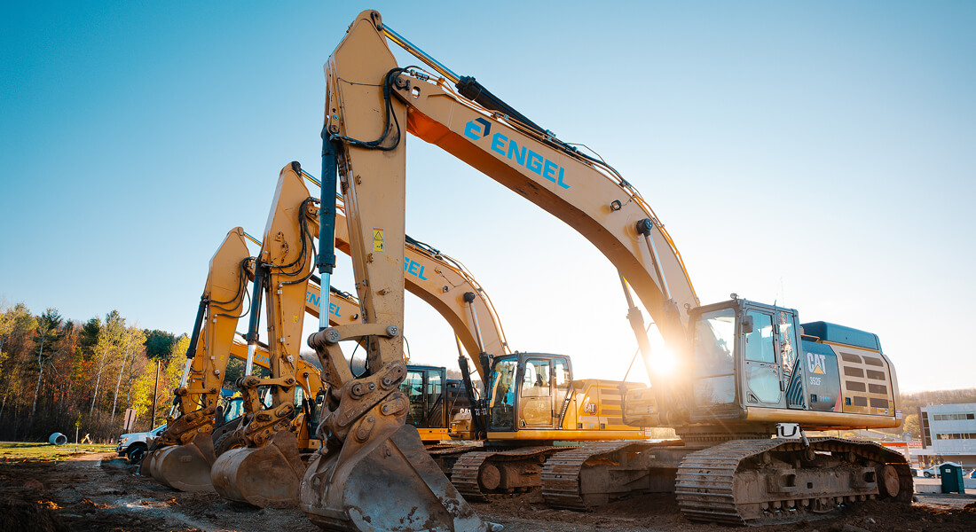 Four excavators parked in sunlight at a construction site.