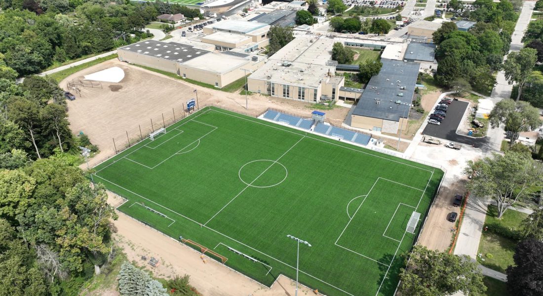 Aerial view of soccer field, trees, buildings, and roads.