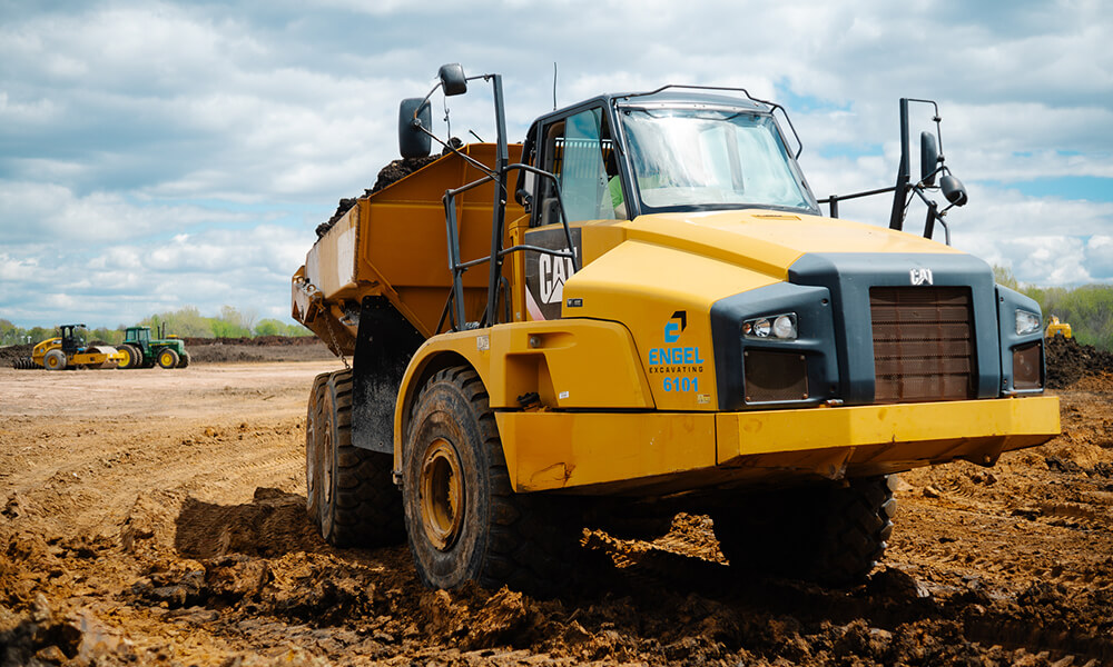 Yellow dump truck with soil at dirt construction site.