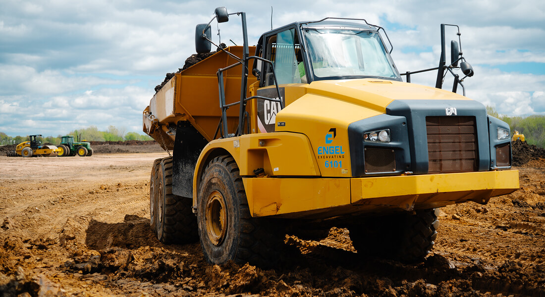 Yellow Caterpillar dump truck with dirt on muddy construction site.