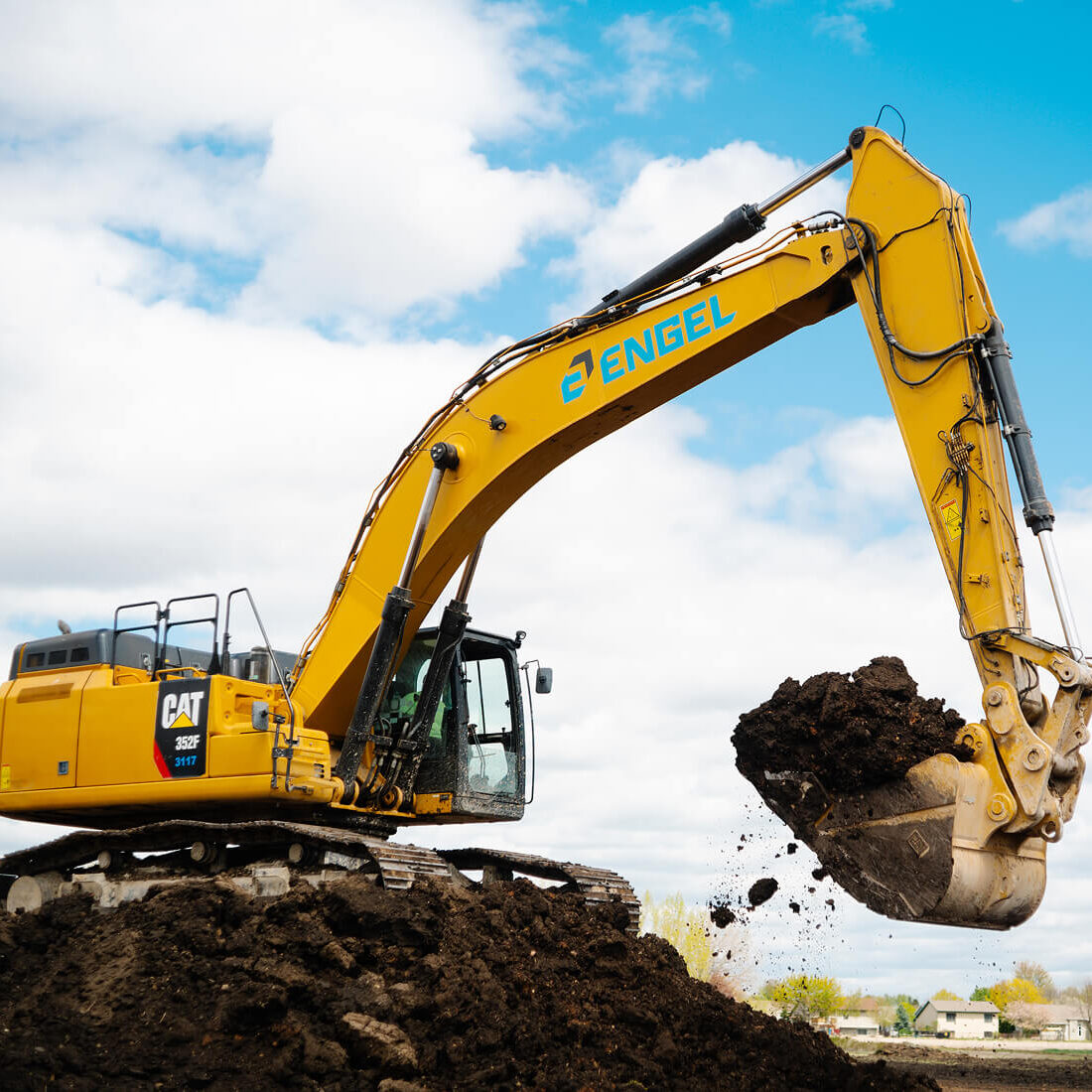 Yellow Engel excavator lifts soil under cloudy sky.