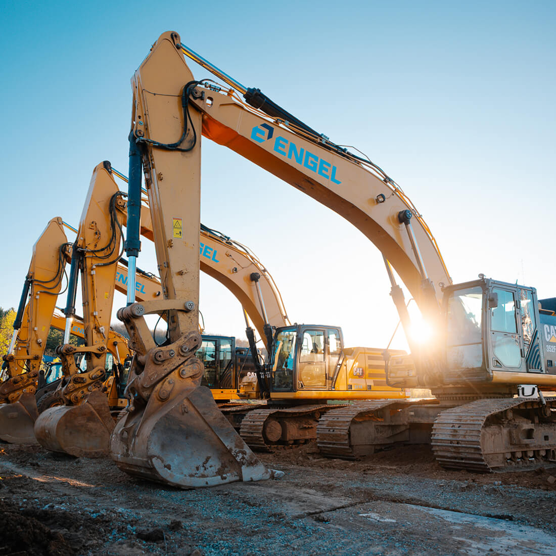 Three yellow Engel excavators parked in sunlight on site.