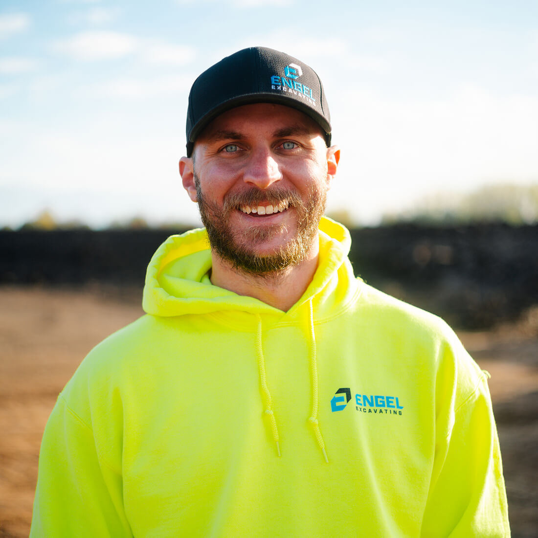 Smiling man in black hat and neon yellow hoodie outdoors.