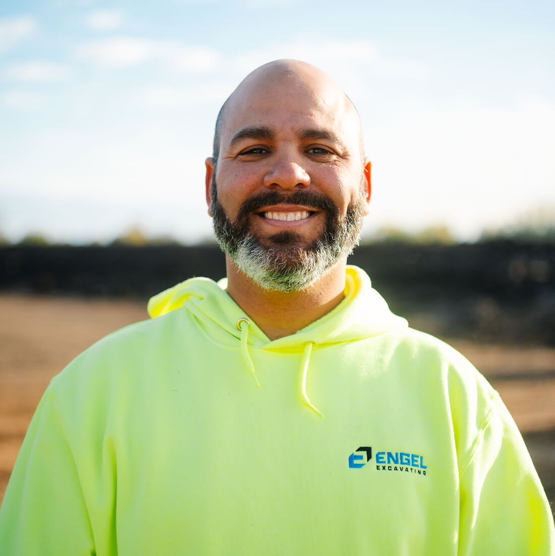 Man in yellow Engel Excavating hoodie smiles outdoors.