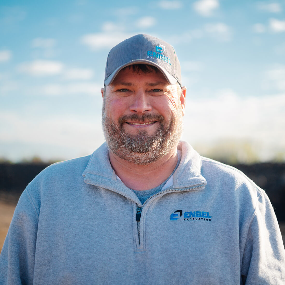 Smiling man in gray Engel Excavating sweatshirt outdoors.
