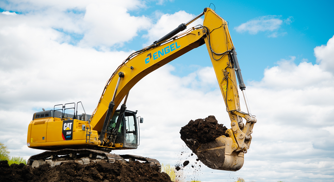 Yellow excavator lifts soil under partly cloudy sky.