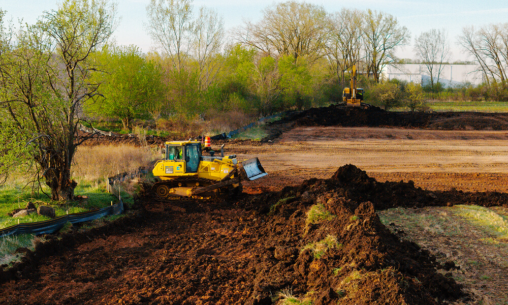 Bulldozers level dirt at a tree-lined construction site.