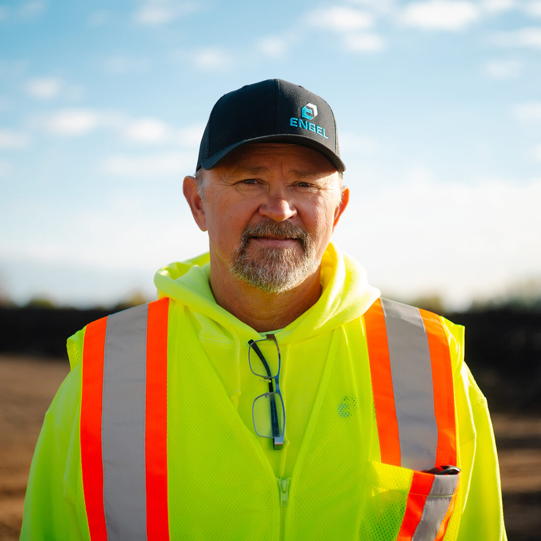 Man in neon vest and cap outdoors with blue sky.