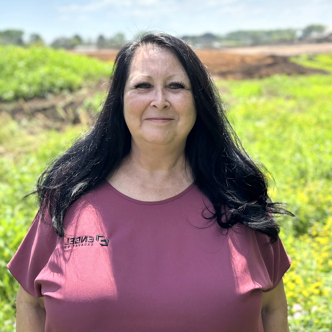 Woman with long dark hair in field wearing mauve shirt.