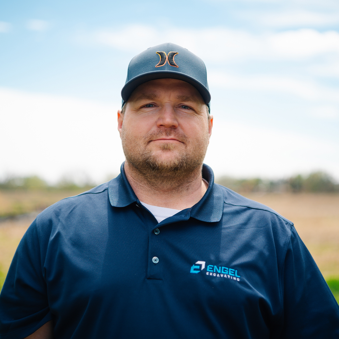 Man in navy polo and black cap outdoors on sunny day.