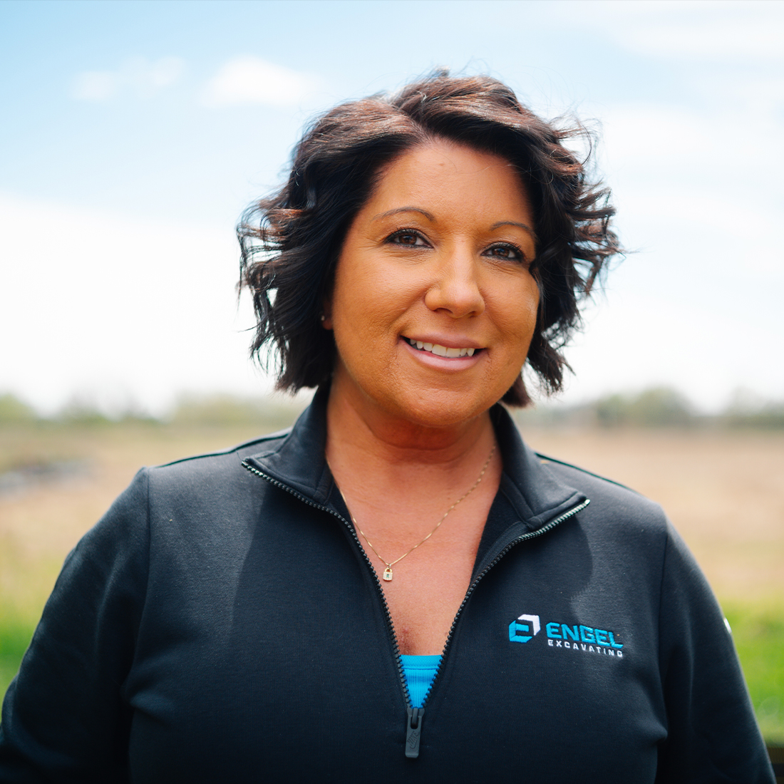 Smiling woman outdoors, field and sky behind.